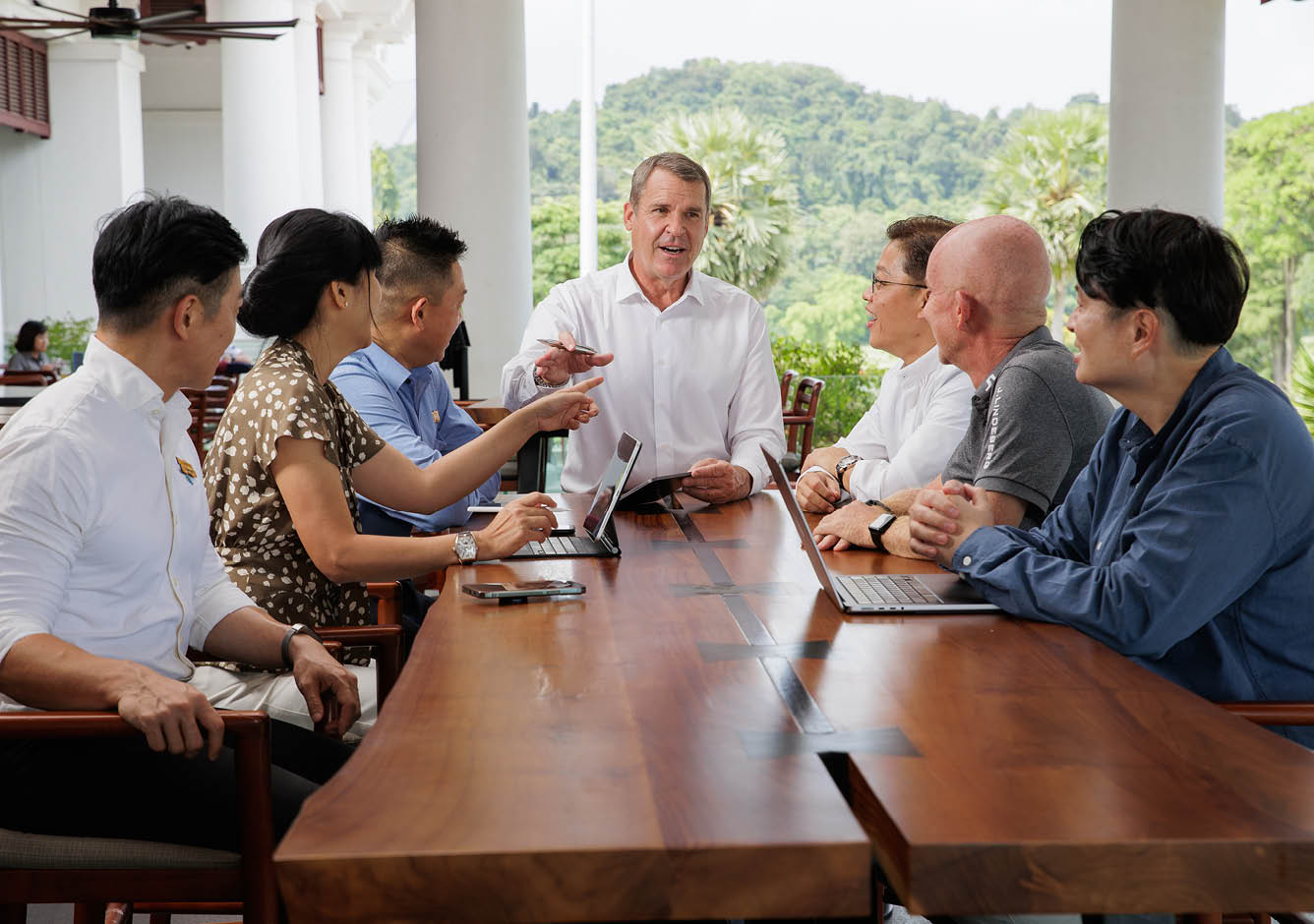 A group of people are sitting around a table with a laptop. AI generated content