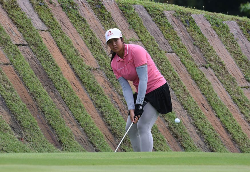 A woman in a pink shirt and white hat is swinging a golf club at a golf ball. AI generated content