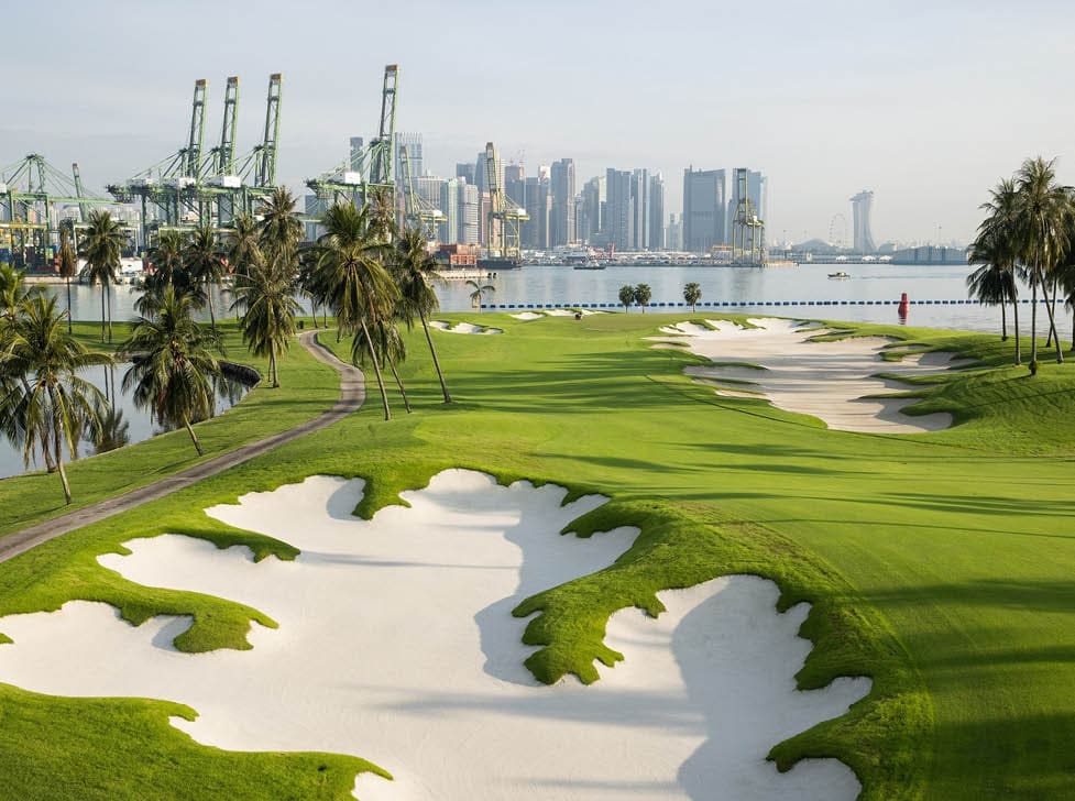 A green golf course with a white sand bunker. Description generated by AI