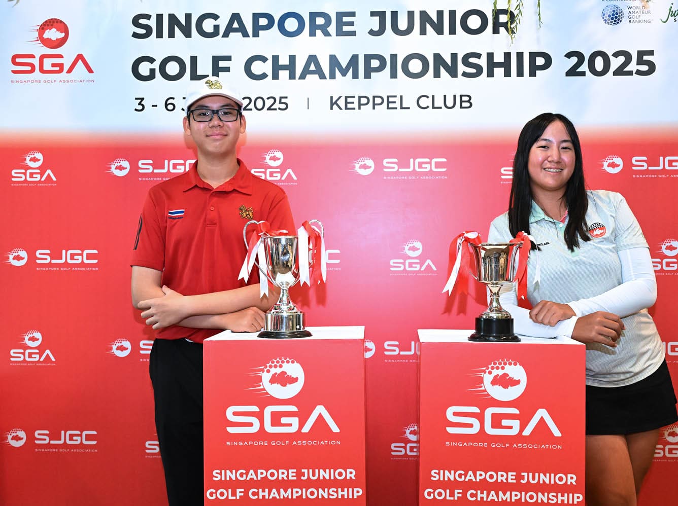 A man and a woman standing in front of a red sign with a golf trophy. Description generated by AI